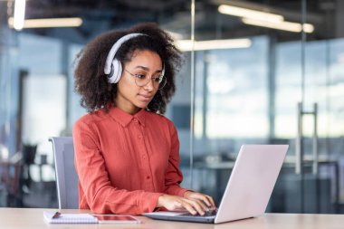Ofisin içinde dizüstü bilgisayarla çalışan ciddi konsantre bir kadın, klavyede kulaklıkla düşünen bir iş kadını, ses podcast 'i dinleyen programcı, eğitim kursu.
