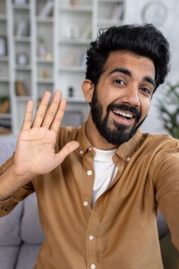 Telefonla konuşan mutlu Hindu adam, kameraya el sallıyor, aile ve arkadaşlarla sohbet ediyor, gülümsüyor, kamera görüntüsü dikey..