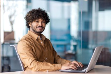 İş yerindeki genç başarılı iş adamının portresi İspanyol asıllı gülümseyen ve kameraya bakan erkek programcı başarı sonuçlarından memnun..