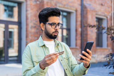 Aldatılmış hayal kırıklığına uğramış adam çevrimiçi para transferi hatası, ofis binası dışında günlük kıyafet giyen iş adamı telefon ve banka kartı, internet dolandırıcısı..