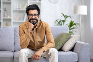 Evdeki kanepede oturan genç bir Hintli 'nin portresi, elini çenesinde dinlendiriyor, özgüvenle ve gülümseyerek kameraya bakıyor..