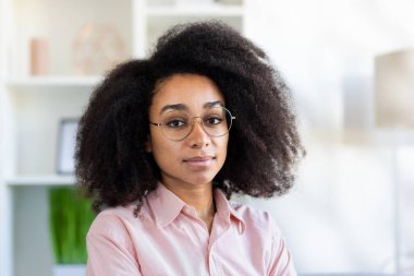 Pembe gömlekli genç bir Afro-Amerikalı iş kadınının yakından çekilmiş fotoğrafı. Kameraya ciddi ve emin bir şekilde bakıyor..