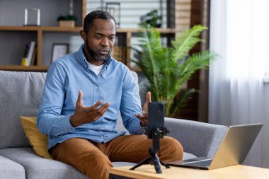 Ciddi konsantre olmuş bir adam internet video kursuna kaydoluyor. Afro-Amerikan bir adam oturma odasındaki koltukta oturuyor..