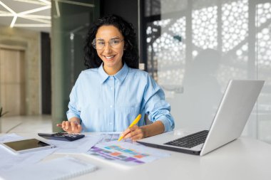 İş yerindeki başarılı genç finansörün portresi, iş kadını masa raporları ve sözleşmeleri dolduruyor, kağıt üzerinde çalışan kadın çalışan bilgisayarla kameraya bakıp gülümsüyor..