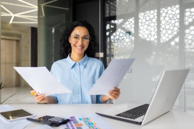 İş yerindeki başarılı muhasebeci kadın kameraya bakıyor, kontrat belgelerini ve raporları tutuyor, iş kadını başarı sonuçlarından memnun..
