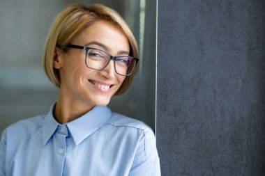 Gözlüklü güzel sarışın iş kadınının yakın plan portresi ofis binasının içinde çalışan ve kameraya gülümseyen bir kadın..