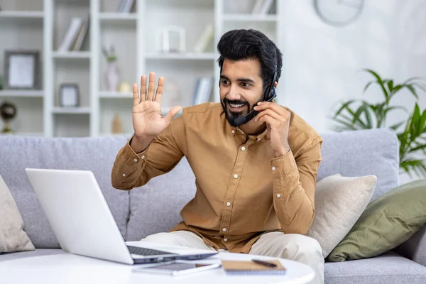 Friendly smiling indian man teacher or freelancer with wireless headset waving to someone having ,remote video call online conference interview or distance education, lesson at home