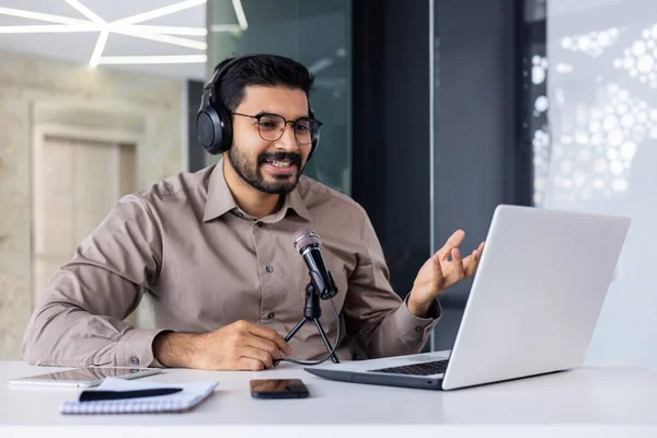 Businessman recording training video online course, man smiling in talking using professional microphone and laptop, working inside office, successful business coach, and financier.