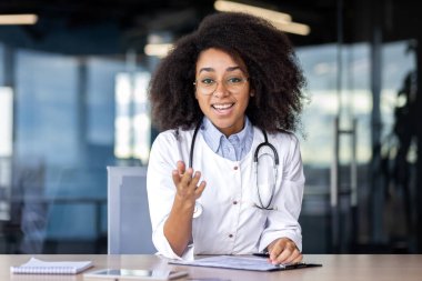 Web kamera görüntüsü, ekran, hastalarla uzaktan konuşan kadın doktor, danışman, kameraya mutlu bir şekilde bakan, elleriyle hareket eden, klinikteki beyaz önlüklü kadın doktor..