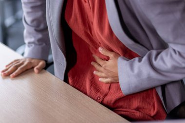 Mide ağrısı, hasta iş kadını karın üstü el ele tutuşması, iş yerinde çalışan kadın ofis içinde dizüstü bilgisayarla çalışıyor..