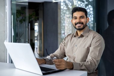 İş yerindeki muhasebeci portresi, iş yerindeki bilgisayarlı iş adamı gülümseyen ve iş yerindeki kameraya bakan, başarı sonuçlarından ve başarılı raporlardan memnun gömlekli adam..