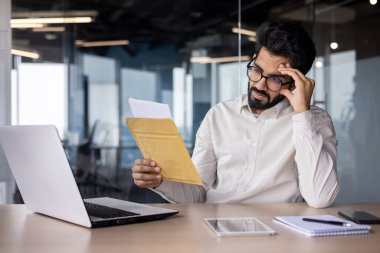 Üzgün işadamı kötü haberlerle dolu bir mektup aldı, iş yerindeki adam üzgün üzgün üzgün bir şekilde masada dizüstü bilgisayarla oturuyor, hüzünlü bir şekilde okuyor..