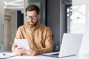 Ofis içinde tablet bilgisayarla çalışan, olgun bir iş adamının bilgisayar kullandığını düşünen, veri okuyan ve çevrimiçi mali verileri kontrol eden ciddi konsantre bir adam..