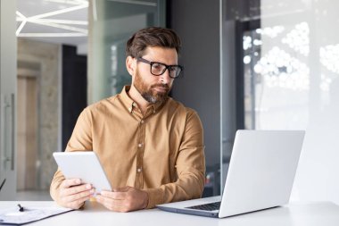 Ofis içinde tablet bilgisayarla çalışan, olgun bir iş adamının bilgisayar kullandığını düşünen, veri okuyan ve çevrimiçi mali verileri kontrol eden ciddi konsantre bir adam..