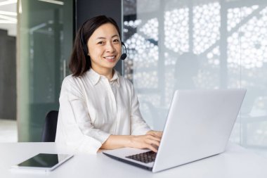 Çevrimiçi destek görevlisinin portresi, kulaklıklı Asyalı kadın gülümseyen ve kameraya bakan, iş yerinde bilgisayarında çalışan iş kadını, çağrı merkezi destek servisi..