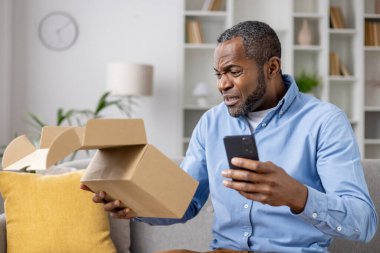 Tatminsiz bir internet alıcısı, yanlış hasarlı paket almış, Afro-Amerikan bir adam oturma odasında, elinde karton kutuyla oturmuş, olumsuz eleştiriler yazıyor..