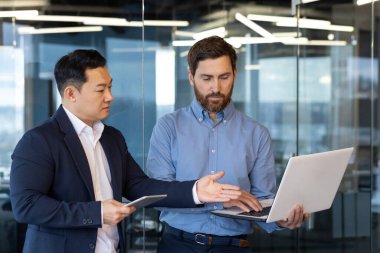 İki genç ırklar arası iş adamı dizüstü bilgisayarda çalışıyor, konuşuyor ve projeyi tartışıyorlar..