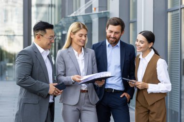 Farklı milletlerden bir grup genç insan, iş adamları ve iş kadınları bir ofis binasının yakınında birbirleriyle konuşuyorlar..