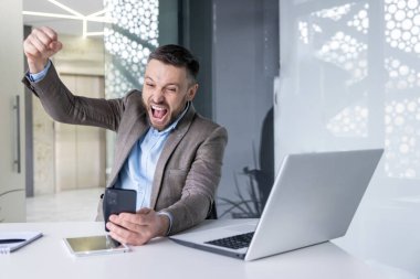 Zaferi kutlayan iş adamı iş yerinde başarılı bir başarı elde etti. Takım elbiseli patron, elinde telefon uygulaması ile zafer tebligatı aldı..