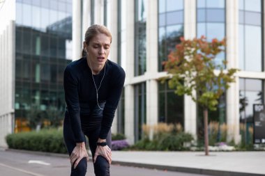 Yorgun sporcu ağır nefes alıyor, uzun koşudan sonra dinleniyor, yaşlı olgun kadın aktif yaşam tarzı, parkın yakınında koşuyor ve formda, telefon ve kulaklık kullanarak ağaçlar müzik dinliyor, podcast yapıyor..