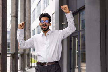 A joyful businessman dances from the outside of the office building, a satisfied man celebrates the victory of Triumph.