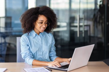 Genç bir Afro-Amerikalı kadın ofiste oturuyor, bilgisayarında çalışıyor ve daktilo yazıyor..