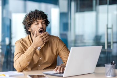 Çok çalışan ve çok yorulan genç iş adamı. Ofisin içinde laptopla çalışıyor. Sıkıcı, uzun, rutin bir iş..