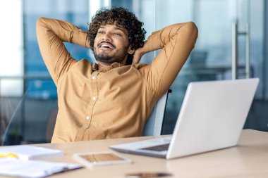 İyi iş adamı başarılı bir şekilde projeyi tamamladı, adam ellerini başının arkasına attı, gülümsüyor memnuniyet, pencere, çalışanların hayalleri, ofis içinde yeni başarılar hakkında düşünüyor.