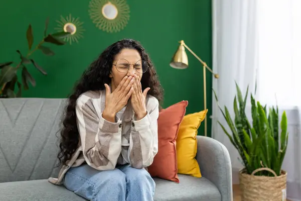 Young woman yawns bored sitting at home on sofa in living room.