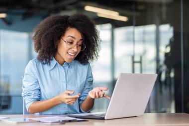 İş yerindeki iş kadını video görüşmesi için dizüstü bilgisayar kullanıyor, çalışan mutlu bir şekilde gülümsüyor ve online bir toplantıda iş arkadaşları ve ortağıyla dostça konuşmalar yapıyor, ofis içinde çalışıyor..