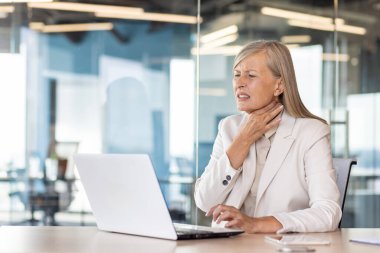 Modern ofis ortamında boğazı ağrıyan, kendini kötü hisseden, boynuna dokunan, stres ve sağlık konsepti olan olgun bir iş kadını..