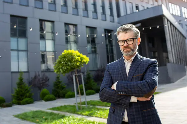 İş yerinin dışında kendine güvenen, kollarını kavuşturan, liderliği somutlaştıran, ciddi bir ifadeye sahip olgun bir yönetici..