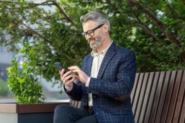 Akıllı telefonuyla meşgul olan takım elbiseli olgun bir şirket çalışanı, hareket halindeki bağlantıyı ve işi resmediyor..
