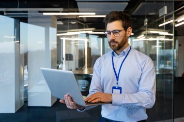 Ciddi bir iş adamı, sistem yöneticisi elinde bir dizüstü bilgisayarla duruyor, tişörtlü düşünen bir adam düşünceli bir şekilde, pencerenin yanında, bilgisayar ile çalışan bir programcı..