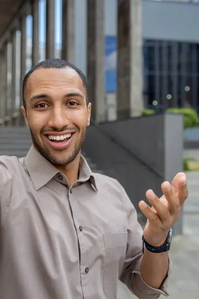 Video call, young man businessman smiling and looking at camera, taking selfie photo, worker walking around city outside office building, using smartphone app for communication, vertical shot.