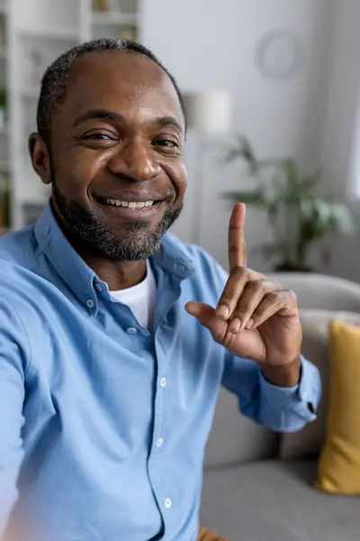 First person view of african american man in casual clothes having video call with friend on modern smartphone. Adult smiling male looking at camera and telling about idea while pointing finger up.