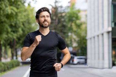 Spor giyimli genç bir adam sabah bir şehir caddesinde koşuyor, yan tarafa bakarken gülümsüyor ve iyi hissediyor. Yakın plan fotoğraf..