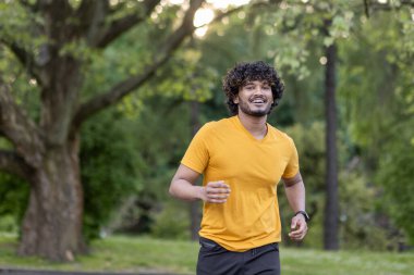 Kıvırcık saçlı enerjik bir Hintli. Huzurlu bir parkta koşuyor. Sağlık ve dayanıklılığı somutlaştırıyor..