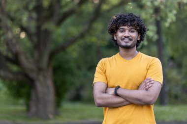 Genç Hintli bir atlet spor yaparken mola veriyor, yeşil bir park ortamında kendine güveni ve canlılığı yayıyor..