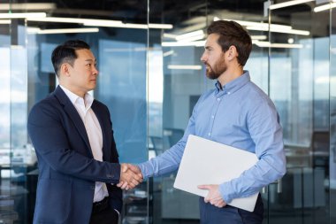 Kurumsal ofis ortamında el sıkışan iki profesyonel işadamı, anlaşma, işbirliği ve takım çalışması anlamına gelir..