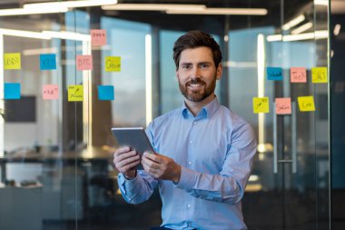 Gülümseyen genç bir işadamının portresi, ofis çalışanı ve mühendislik müteahhidi elinde tablet, kameraya güvenle gülümsüyor..