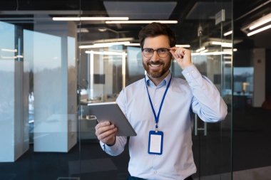 Olgun deneyimli programcı sistem yöneticisi portresi, elinde tablet bilgisayarla gülümseyen ve kameraya bakan adam, iş yerindeki yeni yazılımı test eden olgun işçi..
