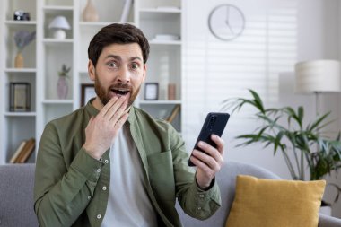 Sersemlemiş beyaz adam elinde akıllı telefonu tutuyor ve kameraya hayretle bakarken ağzını eliyle kapatıyor. Etkilenmiş bir adam cep telefonundaki beklenmedik mesajlara tepki gösteriyor.