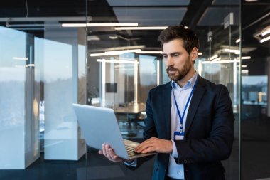 Modern bir ofiste çalışan olgun bir iş adamı laptopundaki verileri analiz ederek liderlik ve kararlılığı temsil ediyor..