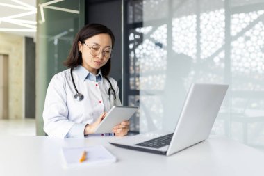 Klinikteki kendini adamış Asyalı doktor çevrimiçi tıbbi danışmanlık ve yardım sağlarken, hastalarla uzaktan ilgilenmeye odaklandı.