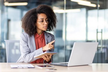 Beyaz yakalı bir işçi ofis malzemeleri, bilgisayar ve dizüstü bilgisayarla çevrili bir masada oturuyor..