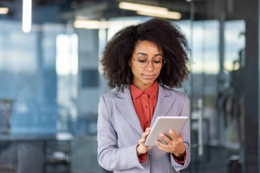 Sarışın televizyon sunucusu ofisteki beyaz yakalı işçi işinde resmi kıyafetlerini giyerken elektrikli mavi tablet kullanıyor..