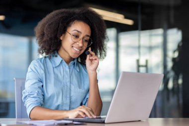 Bir kadın, masa başında dizüstü bilgisayar kullanıyor. Etrafı ofis malzemeleriyle çevrili..