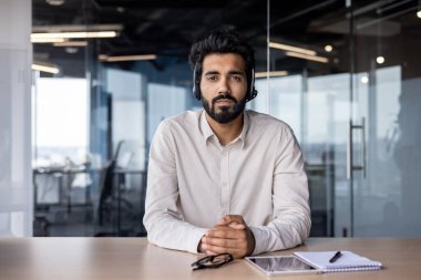 Kendine güvenen Hintli işadamı, kulaklık takıyor. Çağdaş bir şirket ofisinde çalışıyor..