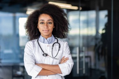 Kollarını kavuşturup kameraya bakan beyaz önlüklü profesyonel aile doktorunun portresi. Tıp alanında önde gelen bir uzman tüm hastaların tamamen iyileşeceğinden emin..